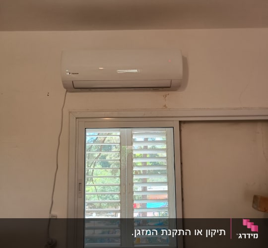 מזגן מותקן מעל חלון עם תריסים